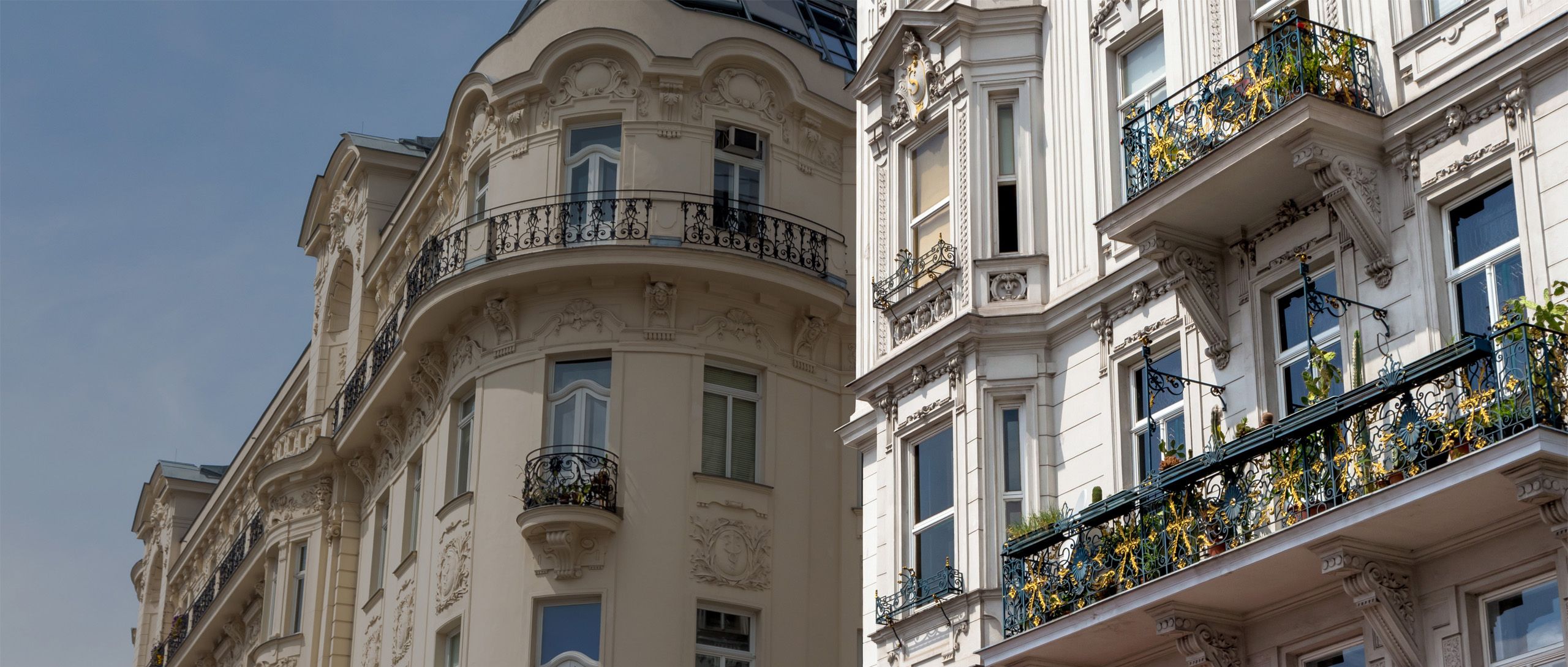 Fassaden von zwei mehrstöckigen Gebäuden mit Balkonen und Verzierungen unter blauem Himmel